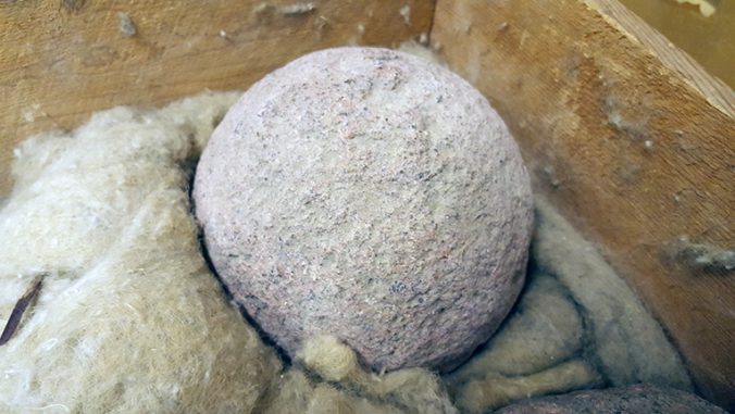 ett foto på en frå kanonkula av sten, liggande på fetvadd i en trälåda