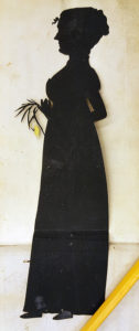 en stående kvinna med en blomma i handen som silhett